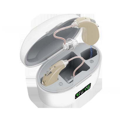 A pair of beige behind-the-ear hearing devices with transparent earpieces and connecting tubes, shown inside an open white charging case on a white background.